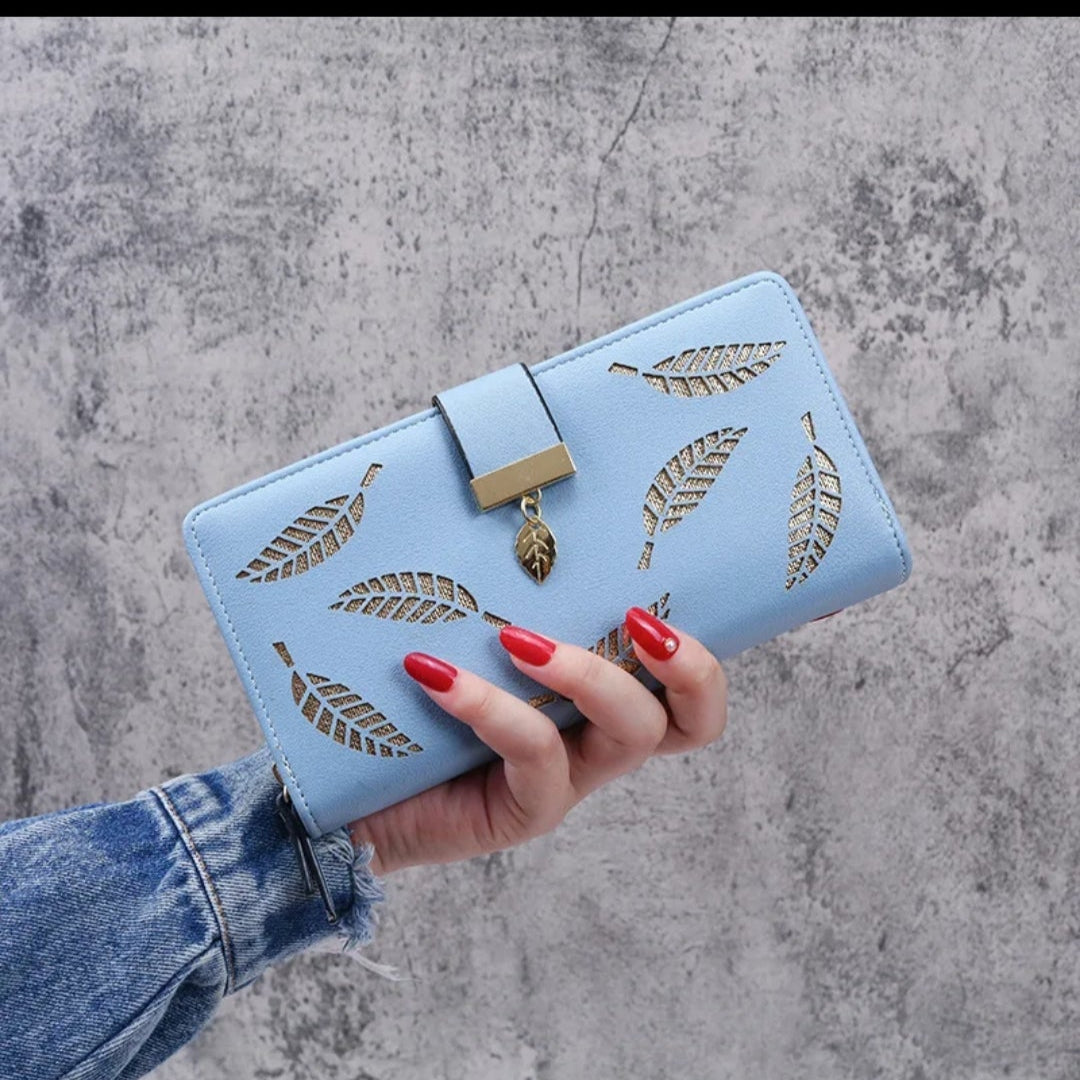 Hand holding a blue wallet with feather designs against a gray concrete background